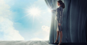 Jeune femme habillée en tailleur qui ouvre ses rideaux pour faire apparaître le soleil